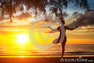 Woman silhouette practicing yoga on the sea beach at sunset