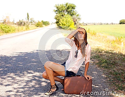 Woman sitting on a suitcase by a countryside road