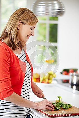 Woman Standing At Counter Preparing Meal In Kitchen