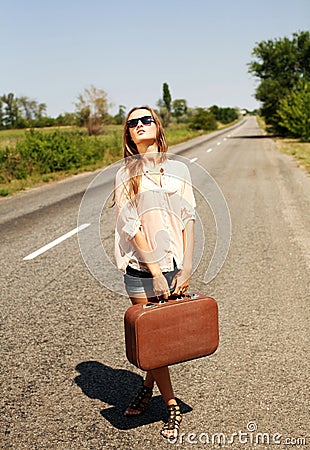 Woman with suitcase, hitchhiking along a countryside road