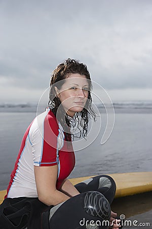 Woman With Surfboard Looking Away While Sitting On Beach