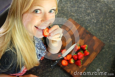 Woman Eating Strawberry While Slicing Fruit