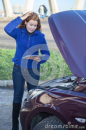 Woman in thought standing near car with tablet pc