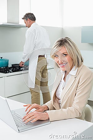 Woman using laptop and man cooking food in kitchen