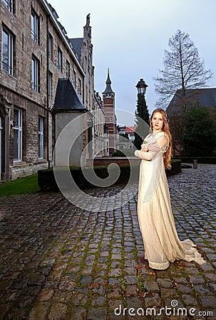 Woman in Victorian dress in a old city square in the evening in profile