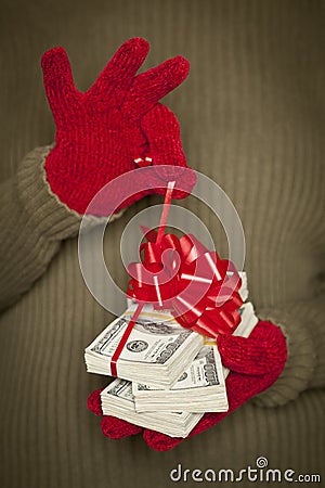 Woman Wearing Mittens Unwrapping Red Bow on Stack of Money