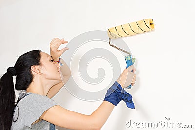 Woman wiping her forehead as she paints a wall