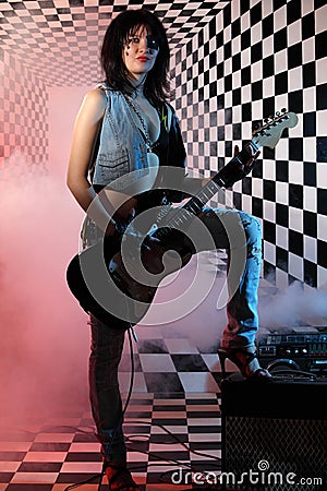 Women with electric guitar stands in studio with checkered background 