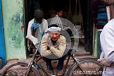 Worker in a turban rests leaning on his retro bicycle on the street
