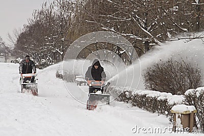 Workers of communal services remove the snow from the sidewalk with the help of motor vehicles