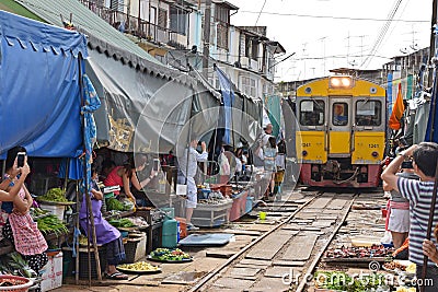 The yellow train has arrived while people are taking pictures and videos at Maeklong Railway Market.