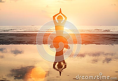 Yoga woman sitting in lotus pose on the beach during sunset, with reflection in water.