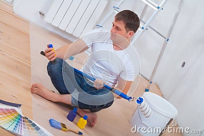 Youg painter sitting on floor holding paintroller