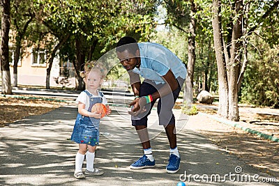 Young African American god father with little girl playing football on nature at summer.