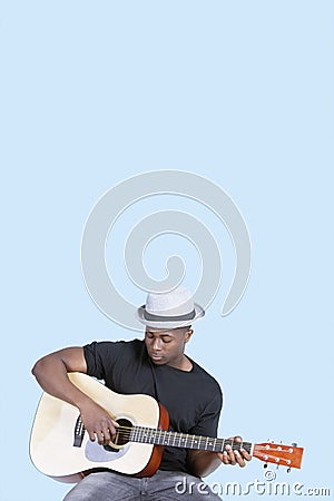 Young African American man playing guitar over light blue background