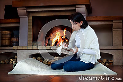 Young attractive woman embroiders by a fireplace