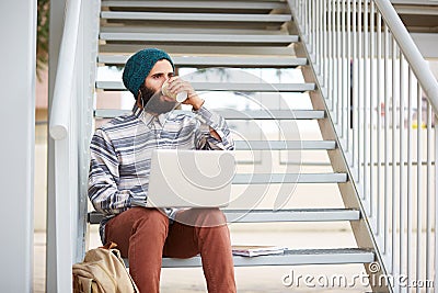 Young bearded hipster student using computer outdoors