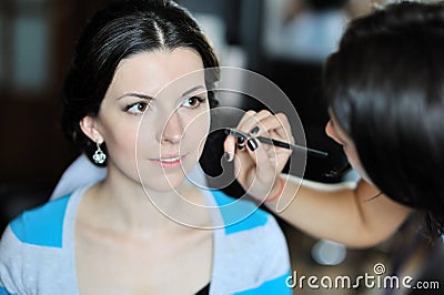 Young beautiful bride applying wedding make-up by make-up artist