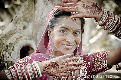 Young beautiful Indian Hindu bride standing under tree with painted hands raised