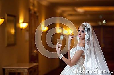 Young beautiful luxurious woman in wedding dress posing in luxurious interior. Gorgeous elegant bride with long veil. Seductive