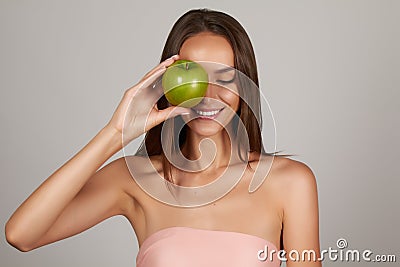 Young beautiful sexy girl with dark curly hair, bare shoulders and neck, holding big green apple to enjoy the taste and are dietin