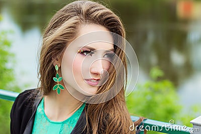 Young beautiful sexy girl in a green dress with beautiful makeup with green shackles sitting on the river Bank in the city