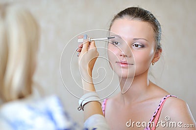Young beautiful woman applying make-up by professional make-up a