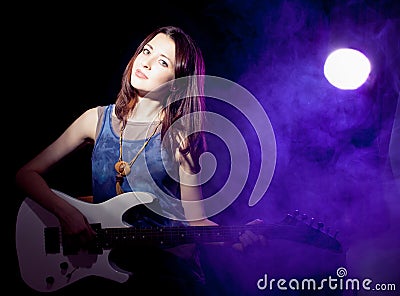 Young beautiful woman on stage with a guitar . Fog on
