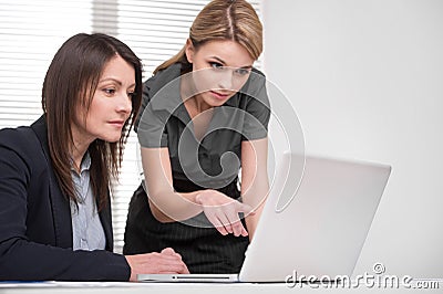 Young blond assistant showing lady boss something on laptop.