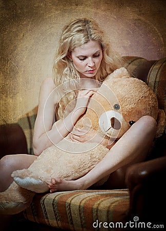 Young blond sensual woman sitting on sofa relaxing with a huge teddy bear