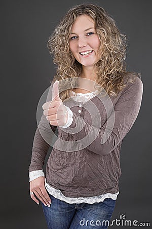 Young blonde woman showing thumbs up on grey background