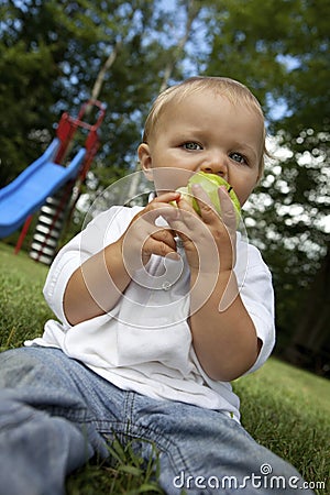 Young boy eating a green apple at the park