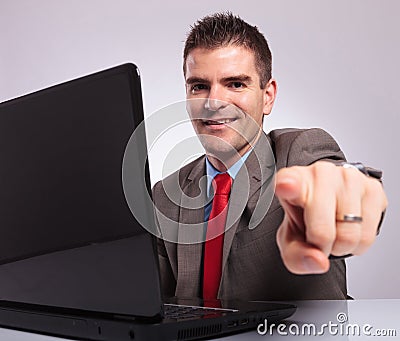 Young business man points at camera while smiling behind laptop