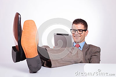 Young business man smiles at tablet, with feet on desk