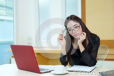 Young business woman thinking with a pen in hand at her workplac