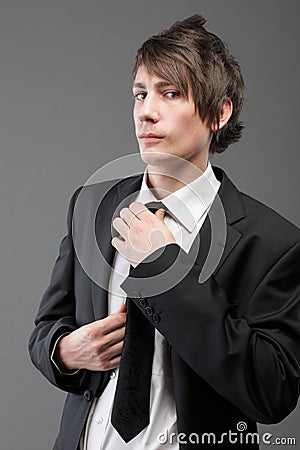 Young businessman black suit casual tie on gray background