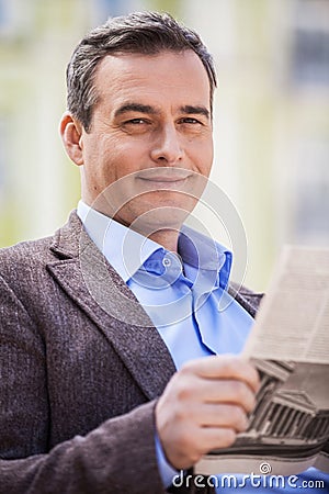 Young businessman reading newspaper while sitting on bench at park