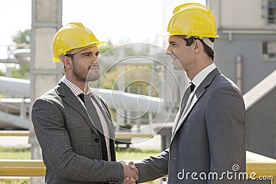 Young businessmen in hard hats shaking hands at construction site