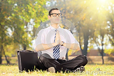 Young businessperson with tie doing yoga seated on grass in a pa