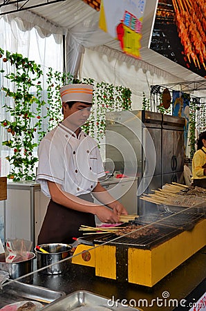 Young chef grills meat and fish on skewers, Singapore