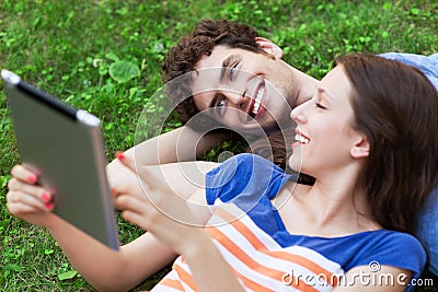 Young couple with digital tablet lying on grass