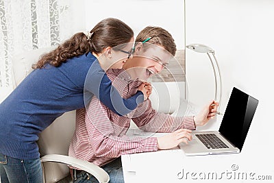 Young couple laughing loud behind the laptop at office