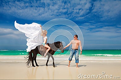 Young couple in love walking with the horse on a tropical beach.