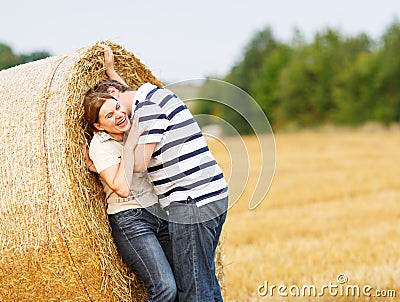 Young couple in love on yellow hay field on summer evening.