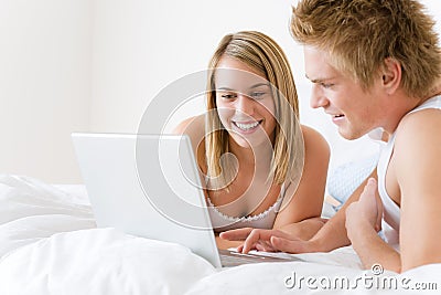 Young couple relax in bed with laptop