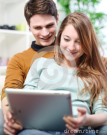 Young couple using digital tablet indoors on the sofa