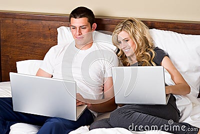 Young couple working on laptops in bed
