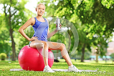 Young female athlete sitting on fitness ball holding a bottle in