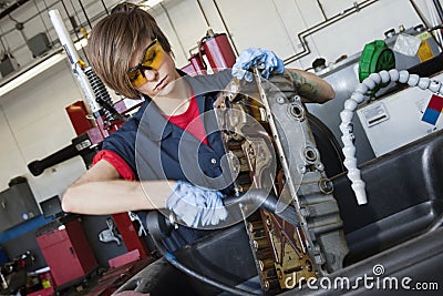 Young female mechanic working with welding torch on vehicle machinery part in auto repair shop