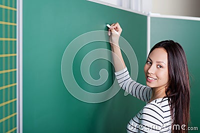 Young female teacher writing on blackboard